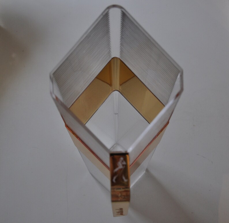 May include: A clear glass pitcher with a gold and brown geometric pattern. The pitcher has a handle with a gold logo.
