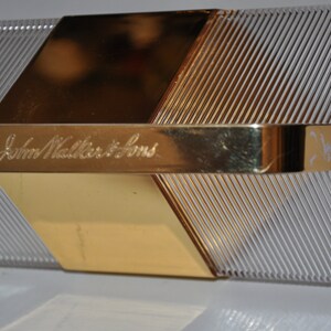 May include: A clear, rectangular box with a gold metal top and a gold metal handle. The box has a textured surface and the words "John Walker & Sons" are engraved on the handle.