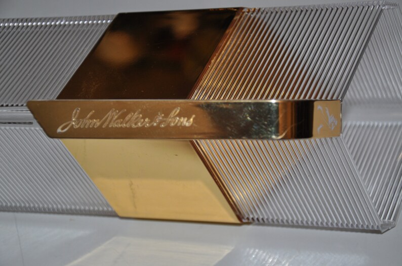 May include: A clear, rectangular box with a gold metal top and a gold metal handle. The box has a textured surface and the words "John Walker & Sons" are engraved on the handle.