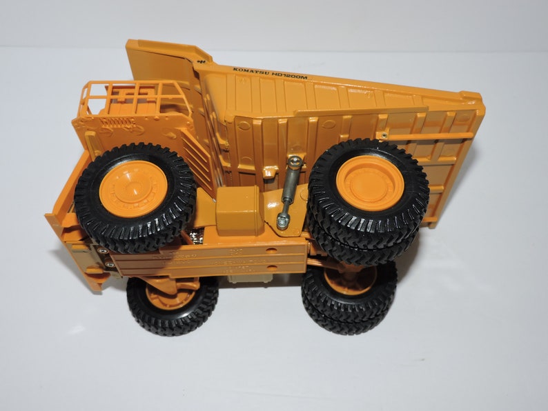 May include: A yellow toy dump truck with black tires and the text "KOMATSU HD402" on the side.