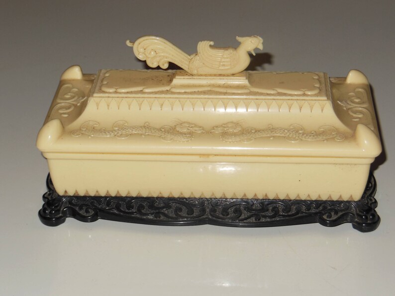 May include: A white ceramic trinket box with a black base. The lid features a raised design of a stylized bird with intricate details.