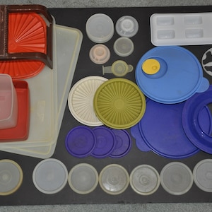 Puede incluir: Una colección de recipientes de plástico de varios tamaños con tapas. Las tapas son en tonos de azul, verde y blanco. También hay varios recipientes de plástico transparentes con tapas.