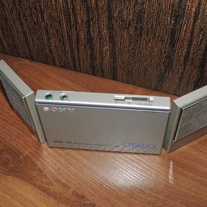 May include: A silver Sony SRS-10 stereo radio with two speakers that fold out. The radio has a volume knob and a headphone jack.