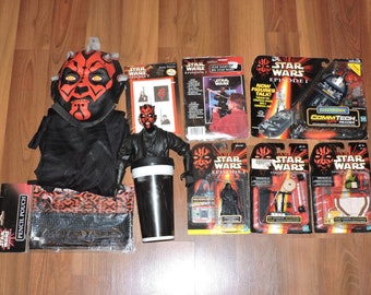 May include: A collection of Star Wars Episode I toys, including a Darth Maul mask, a Darth Maul action figure, a pencil pouch, a travel mug, and several action figure packaging featuring Darth Maul, Qui-Gon Jinn, and other characters.