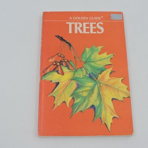 May include: A Golden Guide book titled "TREES" with an orange cover. The cover features a detailed illustration of green and yellow maple leaves and seed pods. The book is a guide to trees.