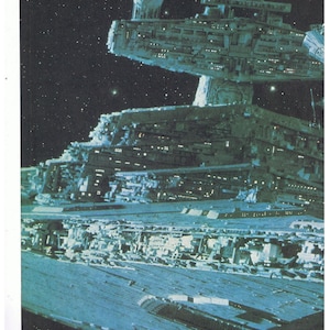 May include: A large, grey spaceship with a detailed exterior, set against a dark, starry background. The spaceship has a large, flat surface and a smaller, cylindrical structure on top.