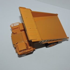 May include: A yellow toy dump truck with the text "KOMATSU" printed on the side. The truck is tilted up, showing the bed of the truck.