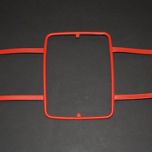 Peut inclure: Un cadre en plastique rouge avec deux barres horizontales, conçu pour tenir une feuille de papier ou une photo.
