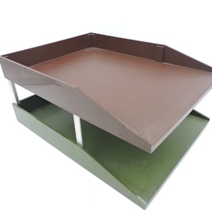 May include: A two-tiered desk organiser with a brown top tray and a green bottom tray. The trays are supported by silver metal legs. The organiser is designed to hold papers and other office supplies.