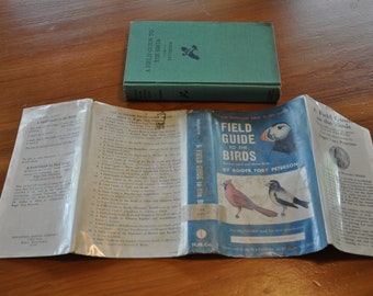 May include: A vintage paperback copy of "A Field Guide to the Birds" by Roger Tory Peterson. The cover features a colorful illustration of a puffin, a cardinal, and a black and white bird. The book is open to the title page and the inside cover.