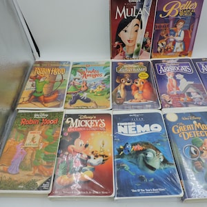Pu&ograve; includere: Una collezione di VHS Disney con film d'animazione come "Mulan", "Robin Hood" e "Alla ricerca di Nemo". Le cassette presentano copertine colorate con illustrazioni dei personaggi e titoli.