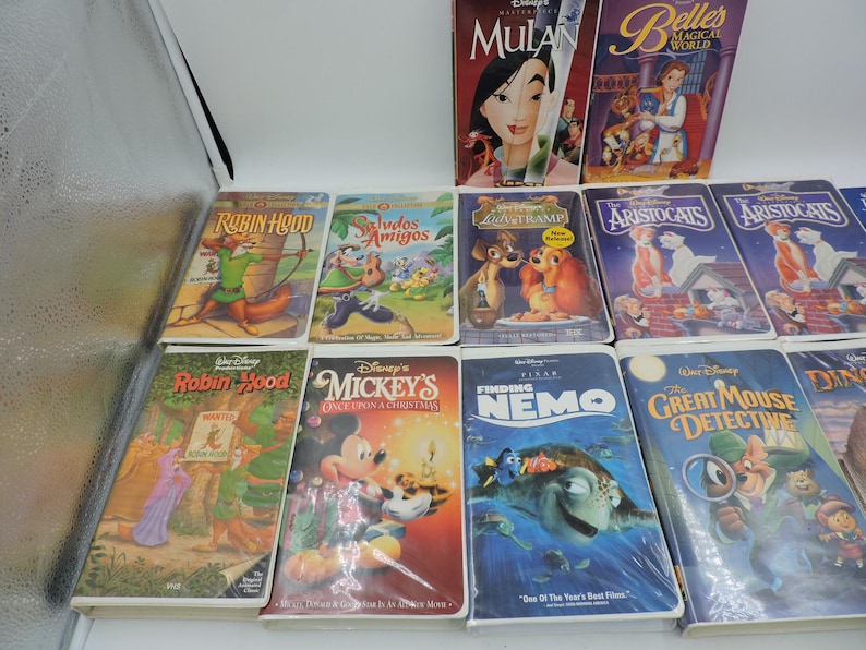 Pu&ograve; includere: Una collezione di VHS Disney con film d'animazione come "Mulan", "Robin Hood" e "Alla ricerca di Nemo". Le cassette presentano copertine colorate con illustrazioni dei personaggi e titoli.