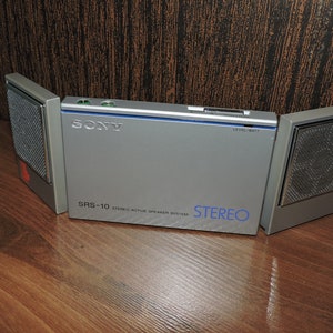 May include: A silver Sony SRS-10 stereo active speaker system with a blue label and the text "STEREO" on the front. The system has two detachable speakers.