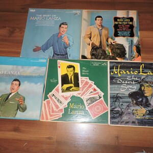 May include: Five vinyl records by Mario Lanza. The records are all in different colours and have different album covers. The covers feature images of Mario Lanza, a man in a desert setting, and a man playing cards. The titles of the albums are "The Best of Mario Lanza", "Mario Lanza For The First Time", "Mario Lanza The Magic Mario", "Mario Lanza And The Sound Of My Heart", and "Mario Lanza The Desert Song".
