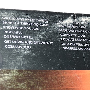 May include: A black and white image of a record album with a list of song titles on the back cover. The song titles include "Wild Winds Are Blowing", "Shape of Things to Come", "Know Who You Are", "Pouk Hill", "One Way Hotel", "Get Down and Get With It", "Cozi Luv You", "Look Not You Don", "Take Me Bak'ome", "Mama Weer All Crazee Now", "Gudbuy T' Jane", "Look At Last Night", "Cum On Feel The Noize", and "Skweeze Me Pleeze Me".