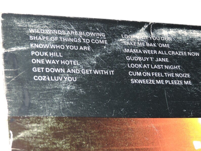 May include: A black and white image of a record album with a list of song titles on the back cover. The song titles include "Wild Winds Are Blowing", "Shape of Things to Come", "Know Who You Are", "Pouk Hill", "One Way Hotel", "Get Down and Get With It", "Cozi Luv You", "Look Not You Don", "Take Me Bak'ome", "Mama Weer All Crazee Now", "Gudbuy T' Jane", "Look At Last Night", "Cum On Feel The Noize", and "Skweeze Me Pleeze Me".