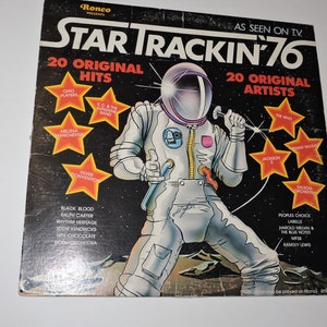 May include: A black and white album cover with a cartoon astronaut in a space suit. The album title is "Star Trackin' 76" with the text "20 Original Hits" and "20 Original Artists". The album cover features a list of artists including Ohio Players, K.C. & The Sunshine Band, Melissa Manchester, Silver Convention, Black Blood, Ralph Carter, Rhythm Heritage, Eddie Kendricks, Hot Chocolate, The Who, Jackson 5,  SalSoul Orchestra, Peoples Choice, Labelle, Harold Melvin & The Blue Notes, M.S., and Ramsey Lewis.