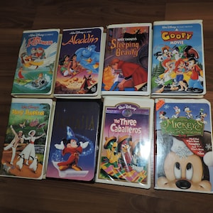 Pu&ograve; includere: Una collezione di otto videocassette VHS Disney, tra cui "The Rescuers", "Aladdin", "Sleeping Beauty" e "A Goofy Movie". Altri titoli sono "Mary Poppins", "Fantasia", "The Three Caballeros" e "Mickey's Twice of Christmas". Le cassette sono su una superficie di legno.