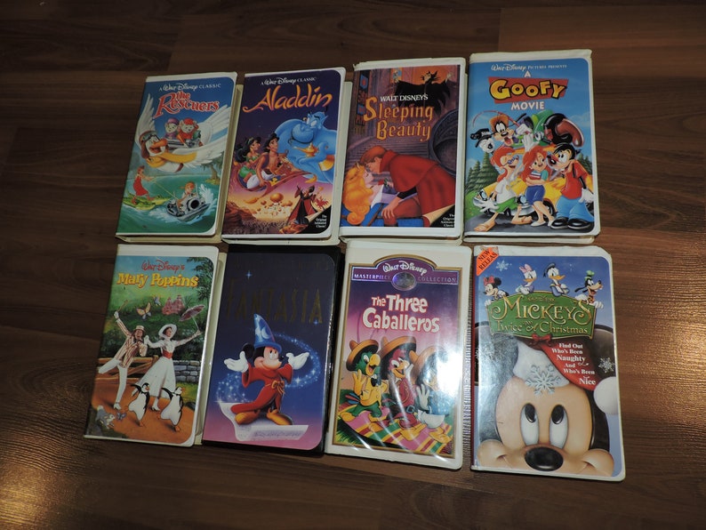 Pu&ograve; includere: Una collezione di otto videocassette VHS Disney, tra cui "The Rescuers", "Aladdin", "Sleeping Beauty" e "A Goofy Movie". Altri titoli sono "Mary Poppins", "Fantasia", "The Three Caballeros" e "Mickey's Twice of Christmas". Le cassette sono su una superficie di legno.