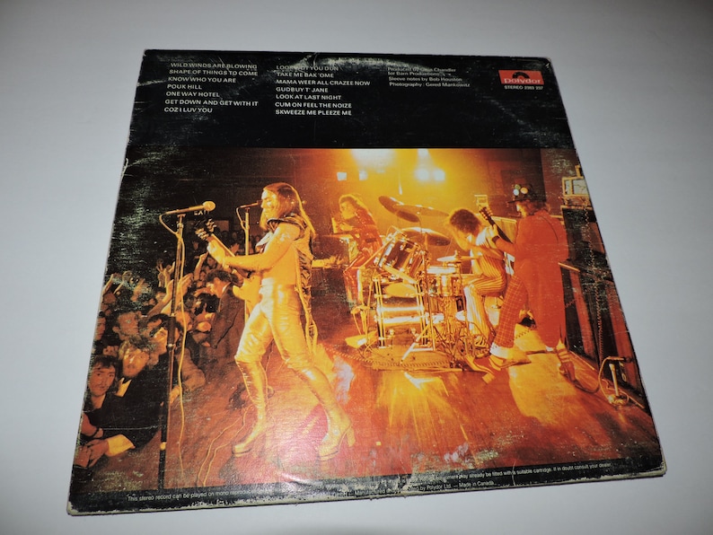 May include: A vintage vinyl record album cover featuring a live performance by a rock band. The band is on stage with a drummer, guitarist, and singer. The album cover is yellowed and has a worn look. The album title is "Wildfire" and the band name is "The Sweet".