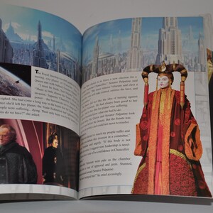 May include: An open book showing a page with a picture of a woman in a red and gold robe. The text on the page reads "The Queen sighed. She had come a long way in the battles to save her people. Since she left her planet, the Trade Federation had been destroying Naboo. Her people were suffering, dying. Their only hope was the Jedi. "What options do we have?" she asked."