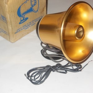 Puede incluir: Un megáfono eléctrico vintage de color dorado, de mano, con un cable negro y una caja blanca con la etiqueta "Panon Electronics of Canada Ltd."