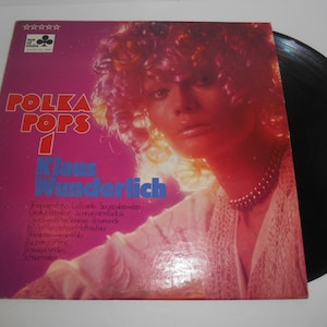 May include: A pink and white vinyl record album cover with a woman on the front. The album is titled "Polka Pops 1" and features the artist "Klaus Wunderlich".