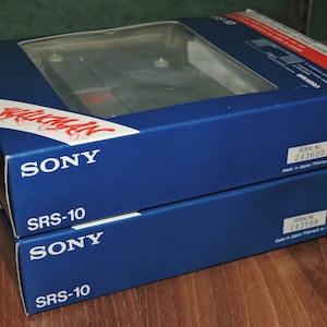 May include: Two blue boxes stacked on top of each other. The top box has the text "SONY" and "SRS-10" printed in white. The bottom box has the text "SONY" and "SRS-10" printed in white. The top box has a serial number of 243600 and the bottom box has a serial number of 243598. Both boxes have the text "Made in Japan/Fabriqu&eacute; au Japon" printed in white.