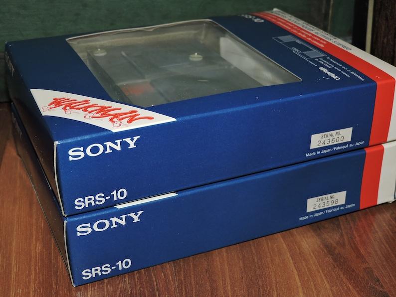 May include: Two blue boxes stacked on top of each other. The top box has the text "SONY" and "SRS-10" printed in white. The bottom box has the text "SONY" and "SRS-10" printed in white. The top box has a serial number of 243600 and the bottom box has a serial number of 243598. Both boxes have the text "Made in Japan/Fabriqu&eacute; au Japon" printed in white.