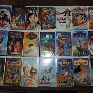 Pu&ograve; includere: Una collezione di videocassette VHS Disney, con titoli come "La Bella e la Bestia", "Mulan" e "Toy Story". Le videocassette presentano opere d'arte e titoli colorati, evocando la nostalgia dei classici film d'animazione.
