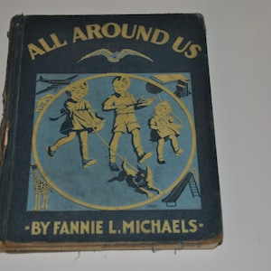 以下が含まれることがあります： 青い背景に黄色い文字で「ALL AROUND US」と書かれた、ビンテージな本の表紙。表紙には、円の中に犬と遊ぶ3人の子供たちの黄色いイラストが描かれている。