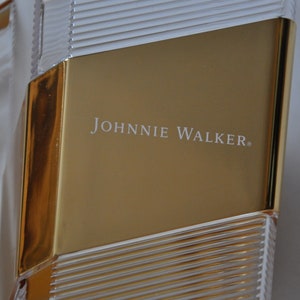 May include: A gold and clear glass bottle with the text "JOHNNIE WALKER" printed on the front.