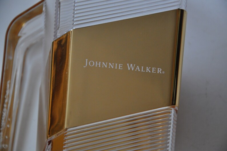 May include: A gold and clear glass bottle with the text "JOHNNIE WALKER" printed on the front.