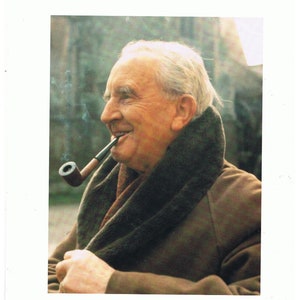 Op de afbeelding: Een portret van een oudere man met wit haar, gekleed in een bruine jas en een donkere sjaal, die een pijp rookt. De man glimlacht en de achtergrond is wazig.