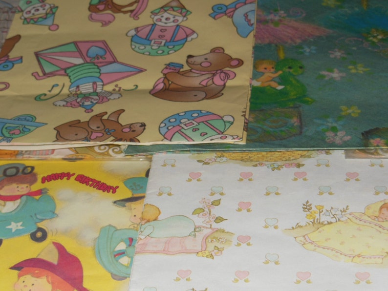 May include: A stack of colourful wrapping paper featuring various designs, including a clown, a teddy bear, a heart-shaped pinwheel, and a baby sleeping in a cot. The paper is ideal for wrapping gifts for birthdays or other special occasions.