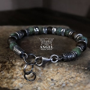 May include: A beaded bracelet featuring green and brown stone beads interspersed with silver-toned metal accents. The bracelet has a lobster clasp closure and a small charm. The brand name "ANGEL ARTISTIC JEWELRY" is visible.
