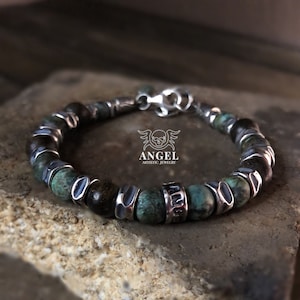 May include: A beaded bracelet featuring turquoise and dark brown stones, accented with silver-toned metal spacers and clasps. The bracelet has the text "ANGEL ARTISTIC JEWELRY" and a skull logo.
