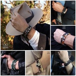 May include: A collection of beaded bracelets in various styles and colors. The bracelets feature a mix of natural stone beads, metal accents, and a central charm. The color palette includes shades of black, gray, brown, and turquoise. The bracelets are shown on wrists.