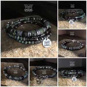 May include: A collection of beaded bracelets featuring a mix of green, brown, and silver beads. The bracelets have a layered design and include a silver charm with the word "ANIOŁ". The bracelets are displayed on a textured surface.