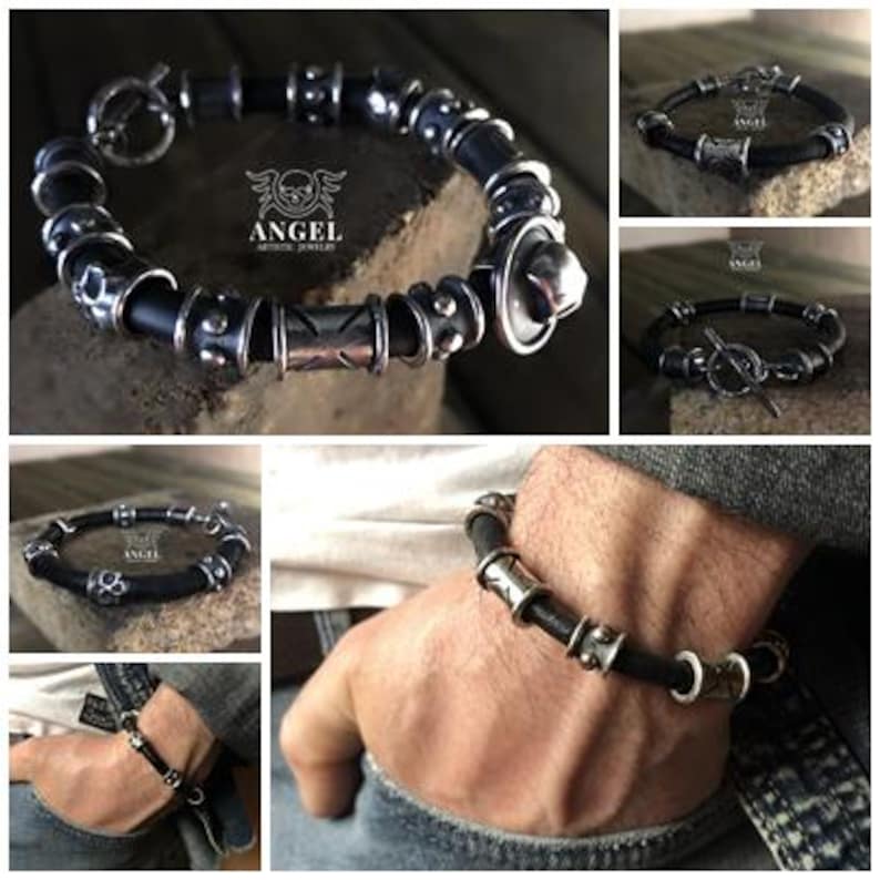 May include: A black leather bracelet with silver-toned metal beads and accents. The bracelet features a toggle clasp and various decorative elements, including patterned and textured beads. The brand logo "ANGEL ARTISTIC JEWELRY" is visible.