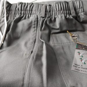 May include: Gray drawstring pants with a large pocket on the right side. The pants have a white drawstring and a tag that reads "Creekwood Outfitters" and "Wear A Pair of Ducks" (Made in U.S.A.).