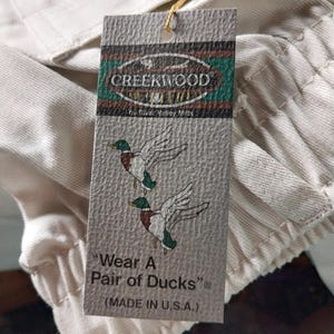 May include: A white tag with brown and green text and a green duck illustration. The tag reads "CREEKWOOD by River Valley Mills" and "Wear A Pair of Ducks" (MADE IN U.S.A.).