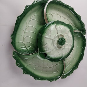 May include: A green and white ceramic serving dish shaped like a lotus flower. The dish has four sections and a lid. The lid has a raised flower design.