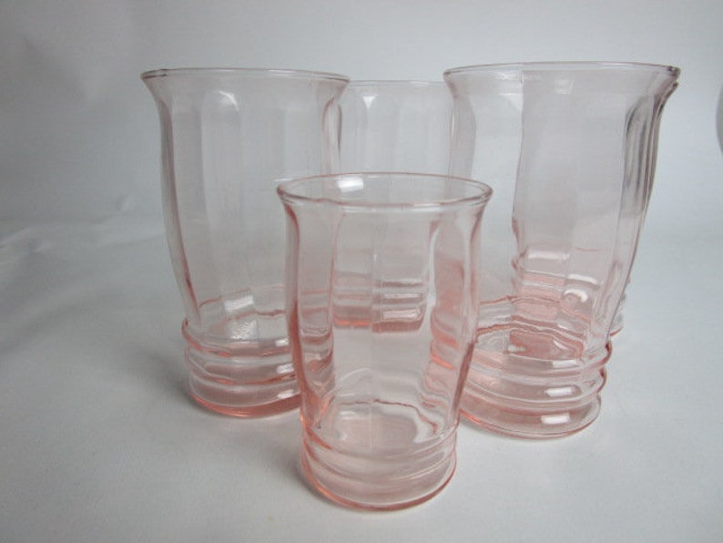 May include: Four vintage pink glass vases of varying sizes. The vases have a ribbed design and flared rims. The glass is a soft, translucent pink. The tallest vase is approximately 18 cm tall. The vases are arranged on a white surface.
