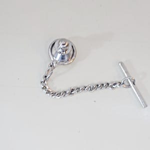 Op de afbeelding: Een zilveren stropdasgesp met een ketting en een T-vormige stang.