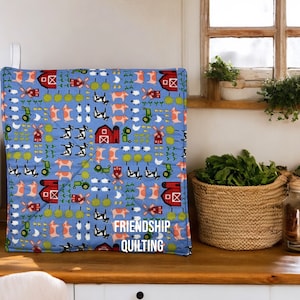 May include: A blue quilted hot pad with a farm animal print. The print features cows, pigs, sheep, chickens, windmills, and red barns. The hot pad has the text "Friendship Quilting" on the bottom.