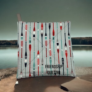 May include: A blue and white fabric pot holder with a pattern of red, white, and blue oars. The pot holder has the text "Friendship Quilting" printed on it.