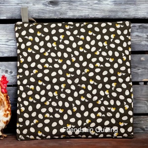 May include: A brown quilted hot pad with a white egg and yellow chick pattern. The text "Friendship Quilting" is printed on the bottom of the hot pad.