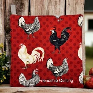May include: Red pot holder with a white and black rooster and hen pattern. The pot holder has white polka dots and the text "Friendship Quilting" in the bottom right corner.