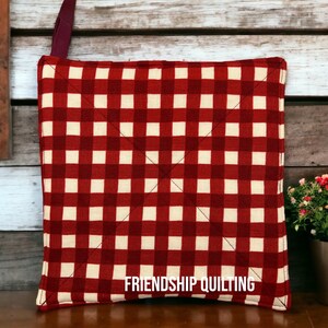 May include: Red and white checkered pot holder with the text "FRIENDSHIP QUILTING" in black.